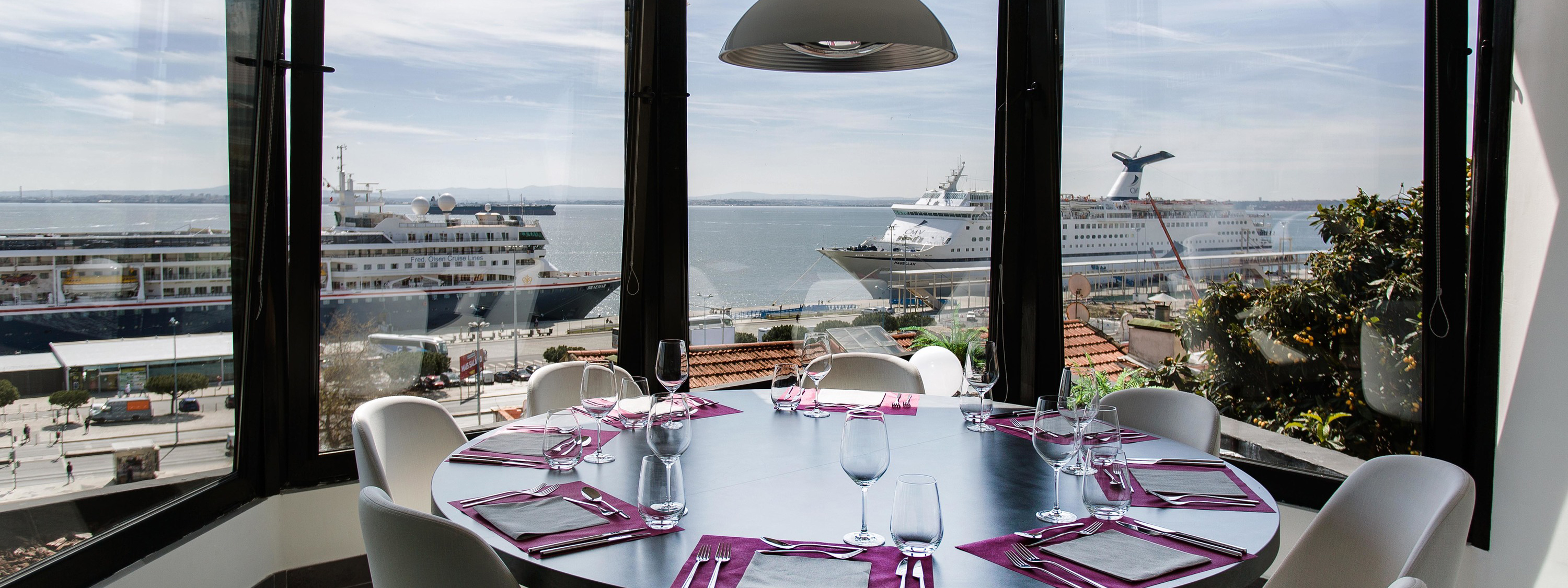 The interior of the Restaurant Faz Figura, with a round table set for a meal, and a window view of the Tagus river.